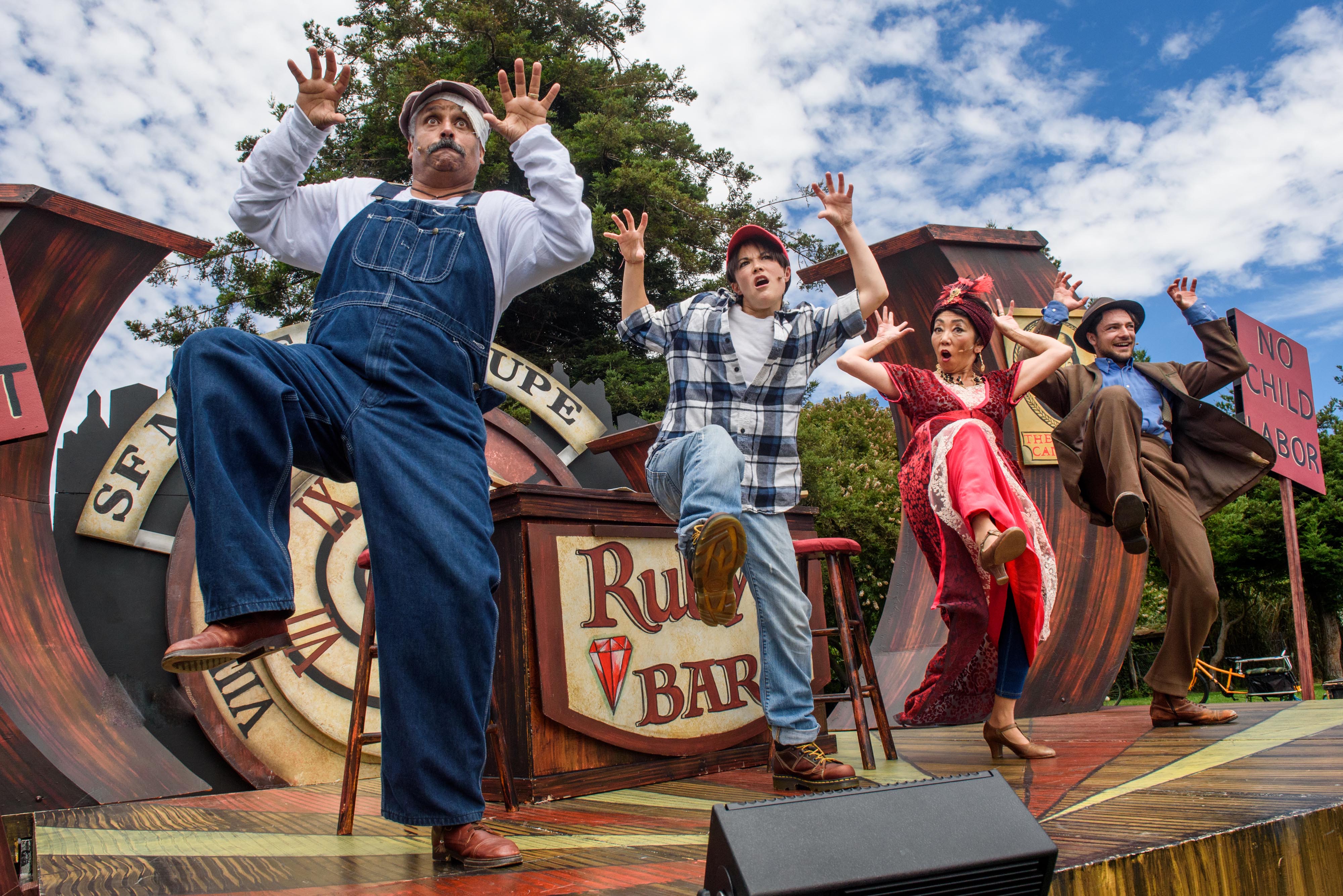 Four mime troupe members dance in unison on an outdoor stage. Bob finds herself on Election Night 1912 in Ruby’s Bar with a group of socialists!