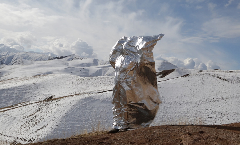 Woman stands in front of a mountain with mylar covering her body