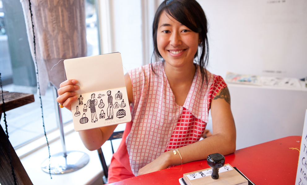 Image of an artist holding up her passport featuring a stamp of her own creation. 