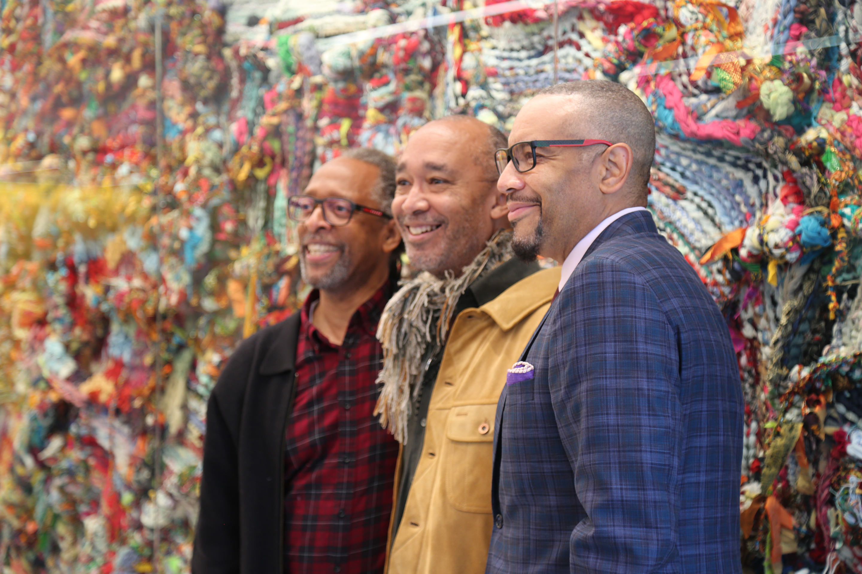 Left to Right: Artists Ron Moultrie Saunders, Ramekon O'Arwisters, and William Rhodes stand in front of "Woven Calm", a sculptural tapestry by O'Arwisters.