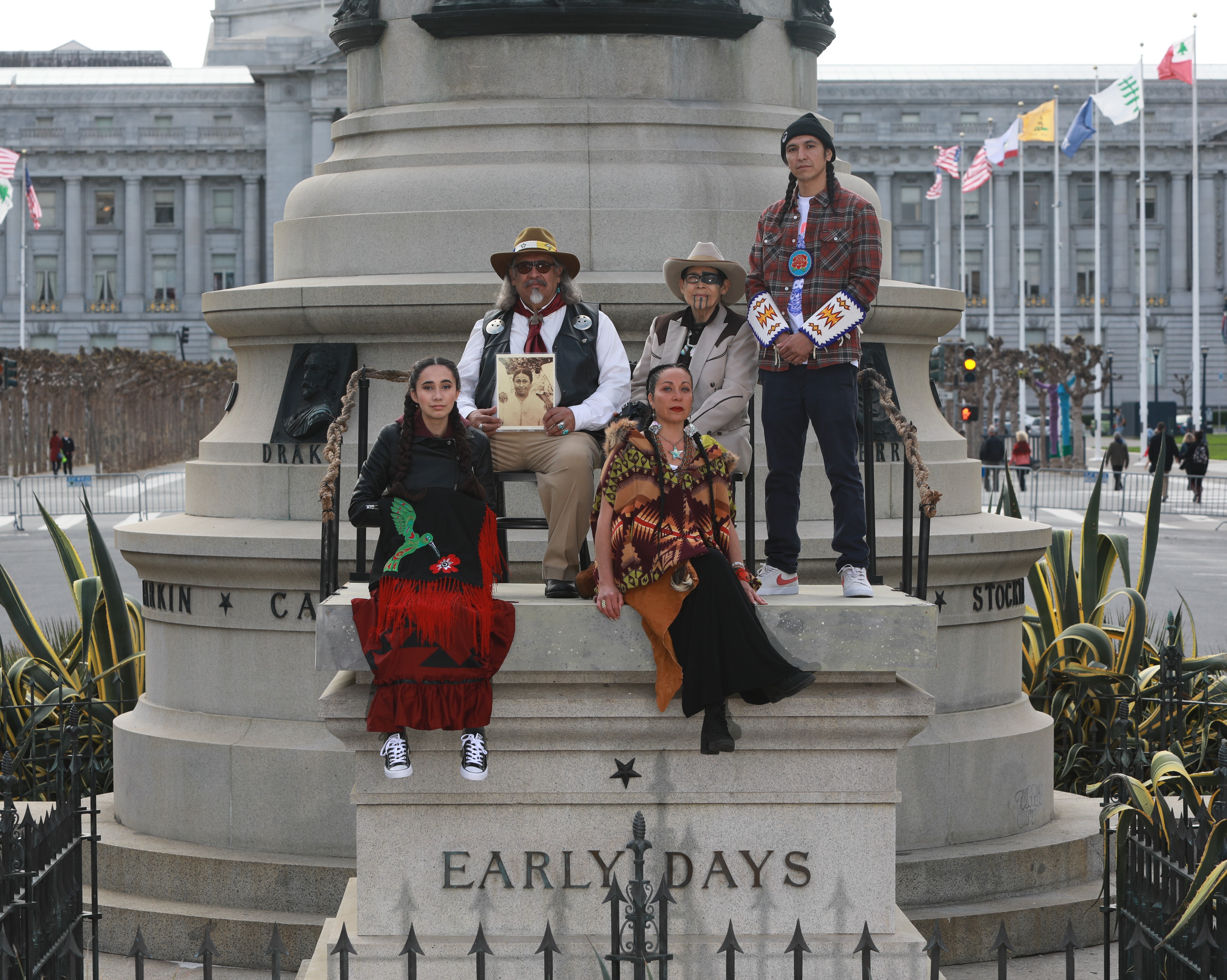 Image of five Native American's on top of the vacated "Early Days" plinth. Seated, front left: Huyana Mumby (Powhatan/KonKow/Tlingit/Kaska Dene) and Tisina Parker (Southern Sierra Miwuk, Mono Lake Paiute, Kashia Pomo). Seated in back left: Emmanuel Montoya (Apache), L. Frank Manriquez (Tongva), and standing, Keith Secola, Jr. (Ute/Ojibwe).